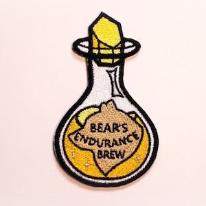 Könnte beinhalten: Gestickter Aufnäher einer Glasflasche mit gelber Flüssigkeit und einem Korkstopfen. Die Flasche ist mit "Bear's Endurance Brew" beschriftet.