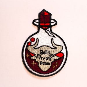 Puede incluir: Una botella de vidrio blanco con un tapón de cristal rojo, llena de un líquido rojo y una silueta de toro blanca. La botella tiene el texto "Bull's Strength Potion" en ella.