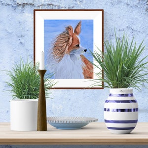 May include: A watercolor painting of a Papillon dog with brown and white fur, looking to the right. The painting is framed in a brown wood frame and is hanging on a blue wall.