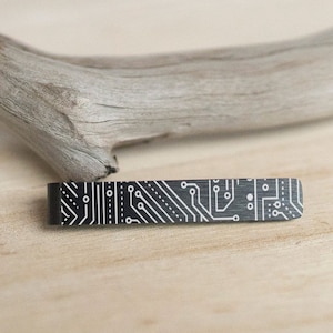 May include: A black tie bar with a white circuit board design.