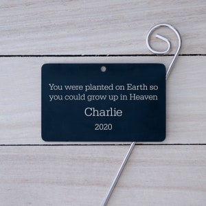May include: Black metal memorial garden marker with the text "You were planted on Earth so you could grow up in Heaven" and the name "Charlie" and the year "2020".
