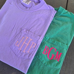 May include: Two t-shirts with pockets, one is lavender with pink embroidered initials "JHP" and the other is green with red embroidered initials "BGM".