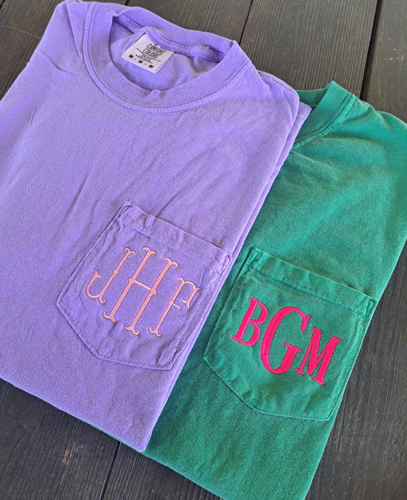 May include: Two t-shirts with pockets, one is lavender with pink embroidered initials "JHP" and the other is green with red embroidered initials "BGM".