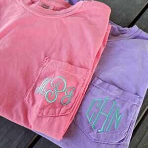 May include: Two t-shirts with embroidered monograms on the front pockets. The top shirt is pink with the monogram "M.P.G." and the bottom shirt is purple with the monogram "C.H.N."