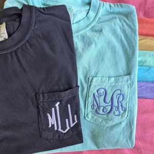 May include: Two t-shirts with pockets, one black and one light blue. Both have embroidered monograms on the pockets. The black shirt has "MLL" in white thread and the light blue shirt has "NYR" in blue thread.
