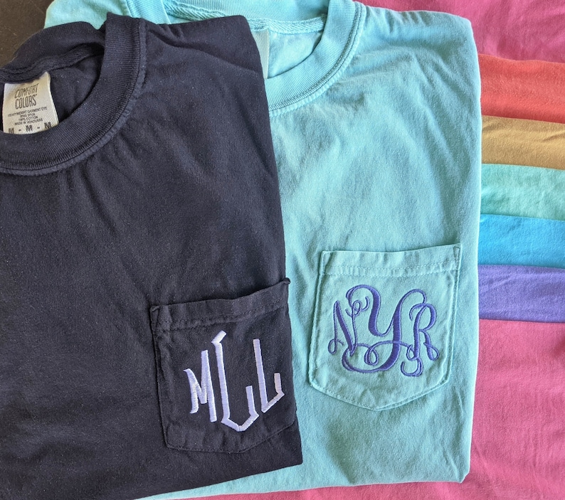 May include: Two t-shirts with pockets, one black and one light blue. Both have embroidered monograms on the pockets. The black shirt has "MLL" in white thread and the light blue shirt has "NYR" in blue thread.