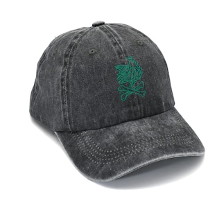 Könnte beinhalten: Eine dunkelgraue, ausgewaschene Baseballkappe mit gebogenem Schirm. Die Kappe hat ein grünes, gesticktes Design eines stilisierten Vogels und gekreuzten Knochen auf der Vorderseite. Die Kappe ist aus weichem, abgenutztem Material.