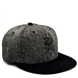 Puede incluir: Una gorra de béisbol negra y gris con un diseño bordado en negro en la parte delantera. La gorra tiene una visera negra y una corona gris.