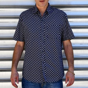 Peut inclure: Chemise à manches courtes bleu marine avec un motif à pois blancs. Le chemisier est porté avec un jean bleu. L'arrière-plan est une surface à rayures horizontales argentées et blanches.