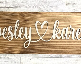May include: A wooden sign with the names "Wesley" and "Karen" written in white cursive lettering, with a heart symbol between the names.