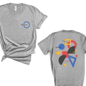 May include: Two heather grey t-shirts. The front of the shirt has a blue circle with the word "Michael" inside. The back of the shirt has a colorful geometric design with blue, red, yellow, and black shapes.
