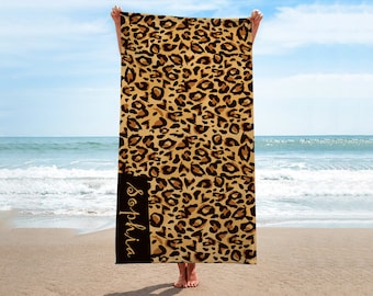 May include: A beach towel with a leopard print design. The towel has a black stripe down the side with the name "Sophia" written in gold lettering.
