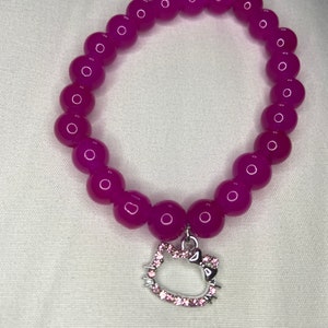 May include: A pink beaded bracelet with a silver Hello Kitty charm. The charm has pink rhinestones.