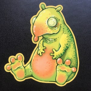 Könnte beinhalten: Eine Cartoon-Illustration eines grünen und gelben Wesens mit einer großen, rosafarbenen Nase und großen, runden Augen. Das Wesen sitzt mit gekreuzten Beinen und hat einen freundlichen Ausdruck.