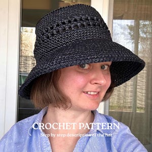 Könnte beinhalten: Ein schwarzer Häkel-Fischerhut mit breiter Krempe und einem dekorativen Lochmusterband um den Kopfbereich. Das Bild enthält den weißen Text CROCHET PATTERN Step by step description of the hat auf einem hellblauen Hemd.