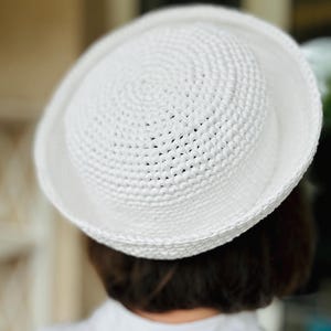 May include: A white, crocheted hat with a rounded crown and a wide brim. The hat is made of a textured, woven material. The hat is a summer accessory.