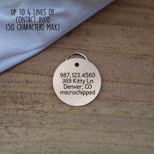 Pode incluir: Uma etiqueta redonda para animais de estima&ccedil;&atilde;o de cor cobre com texto gravado. O texto diz: "987.123.4560 369 Kitty Ln Denver, CO microchipped".
