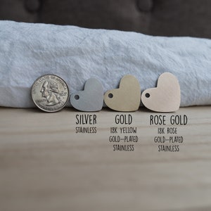 May include: Three heart-shaped metal tags in silver, gold, and rose gold. The tags are labeled "Silver Stainless", "Gold 18k Yellow Gold-Plated Stainless", and "Rose Gold 18k Rose Gold-Plated Stainless".