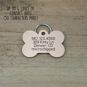 May include: A copper-colored bone-shaped dog tag with a silver ring. The tag has the following text engraved on it: 987.123.4560, 369 Kitty Ln, Denver, CO, microchipped.