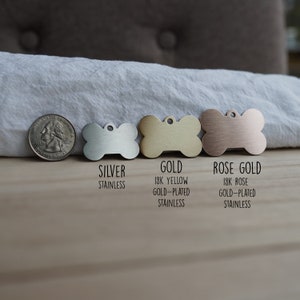 May include: Three dog tags in the shape of a bone, one silver, one gold, and one rose gold. The tags are labeled "Silver Stainless", "Gold 18K Yellow Gold-Plated Stainless", and "Rose Gold 18K Rose Gold-Plated Stainless".