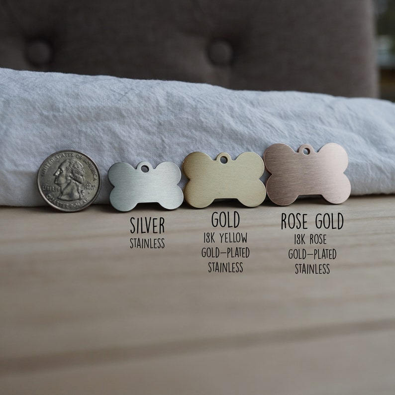 May include: Three dog tags in the shape of a bone, one silver, one gold, and one rose gold. The tags are labeled "Silver Stainless", "Gold 18K Yellow Gold-Plated Stainless", and "Rose Gold 18K Rose Gold-Plated Stainless".