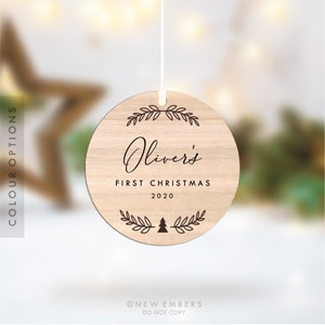K&ouml;nnte beinhalten: Ein runder Holzanh&auml;nger mit brauner Holzmaserung. Der Anh&auml;nger zeigt ein Kranzdesign mit dem Text "Oliver's First Christmas 2020" und einen kleinen Weihnachtsbaum.
