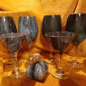 Op de afbeelding: Set van zes handgeschilderde wijn- en martini glazen met een zwart, wit en teal marmerpatroon. Een klein flesje met een kurkstop is ook inbegrepen, met hetzelfde marmerpatroon.