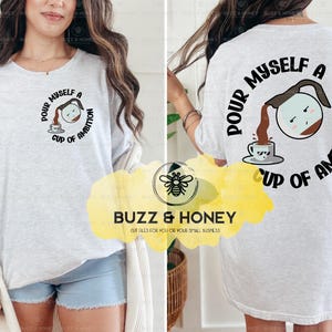 May include: A white t-shirt with a black graphic design of a coffee pot pouring coffee into a cup. The text on the shirt reads "Pour myself a cup of ambition".