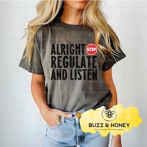 Puede incluir: Una camiseta gris con el texto "Alright Stop Regulate And Listen" en letras negras. Una señal de stop roja está por encima de la palabra "Regulate".