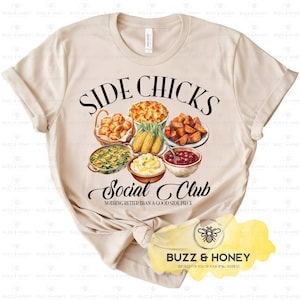 May include: A beige t-shirt featuring the text "SIDE CHICKS SOCIAL CLUB" in black script above illustrations of various side dishes. The phrase "Nothing better than a good side piece" is below the club name. A yellow and white logo is at the bottom.