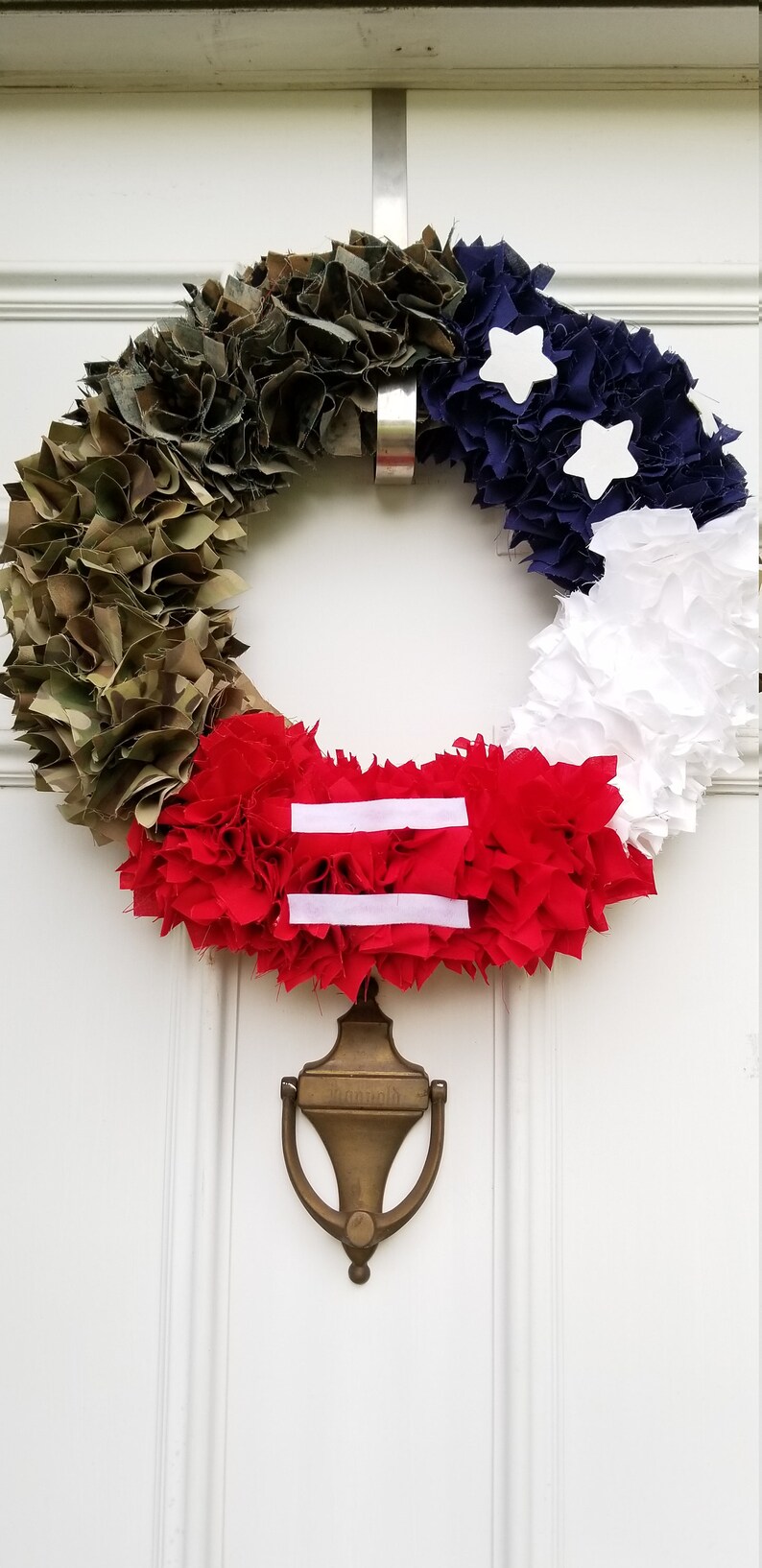 Puede incluir: Una corona patri&oacute;tica con una combinaci&oacute;n de colores camuflaje, azul marino, blanco y rojo. La corona est&aacute; adornada con estrellas blancas y una secci&oacute;n roja con dos rayas blancas. Debajo, un aldaba de lat&oacute;n.