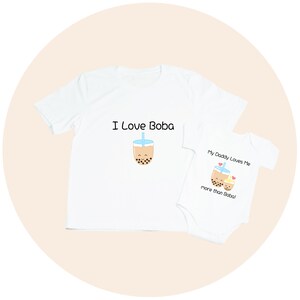 May include: White t-shirt with "I Love Boba" text and a cartoon boba tea graphic. A white baby onesie with "My Daddy Loves Me more than Boba!" text and a matching boba tea graphic.
