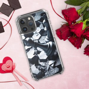 Peut inclure: Coque de téléphone transparente avec un motif d'échecs en noir et blanc. L'image montre une pièce d'échecs tombée sur une surface fissurée, avec d'autres pièces en arrière-plan. La coque est posée sur un fond rose avec des roses rouges et du chocolat.