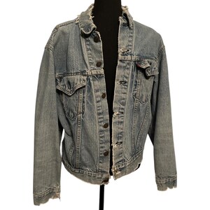 May include: A light blue denim jacket with a button closure and frayed edges. The jacket has a classic design with two front pockets and a single chest pocket.