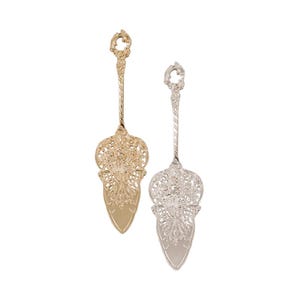 May include: Two cake servers, one in a gold-tone finish and one in a silver-tone finish. Each server features an ornate, intricate filigree handle and a wide, triangular blade with a decorative cutout pattern at the base of the handle.
