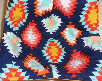Peut inclure: Un porte-pot en tissu bleu avec un motif géométrique dans des tons de rouge, orange, jaune, blanc et turquoise.