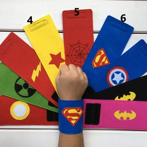 Può includere: Nove braccialetti in feltro con diversi loghi di supereroi, tra cui Superman, Batman, Spiderman e Capitan America. I braccialetti sono rossi, gialli, verdi, blu, neri e rosa.