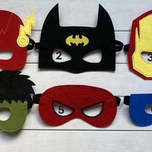 Könnte beinhalten: Sechs Filz-Superheldenmasken in verschiedenen Farben und Designs. Die Masken sind von 1 bis 6 nummeriert. Die Masken sind für Kinder und aus Filz.
