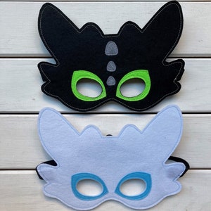 May include: Two felt dragon masks, one black with green eyes and one light blue with blue eyes.