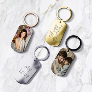 Peut inclure: Quatre porte-clés personnalisés avec des anneaux en métal. Un porte-clés présente une photo d'une personne faisant un bisou, un autre porte l'inscription "Happy Birthday", et un troisième dit "My Love". Le quatrième porte-clés a une photo d'un homme et d'un enfant.