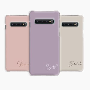 May include: Three clear phone cases with different coloured backgrounds and personalised names. The first case is pink with the name "Stephanie" in gold lettering. The second case is purple with the name "Beth" in white lettering. The third case is beige with the name "Edietha" in black lettering.