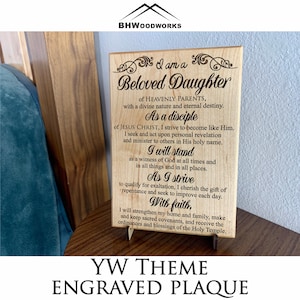 May include: Wooden plaque with engraved text, including "Beloved Daughter" and "YW THEME ENGRAVED PLAQUE." The plaque is displayed on a small stand. The text is in a decorative font.