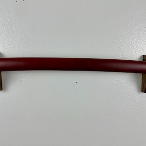 May include: A red katana sword mounted on a wooden wall mount. The sword is displayed horizontally with the blade facing the viewer.