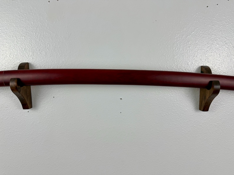 May include: A red katana sword mounted on a wooden wall mount. The sword is displayed horizontally with the blade facing the viewer.