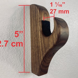 May include: A dark brown wooden wall mount hook with a 1 1/16 inch (27 mm) projection and a 5 inch (12.7 cm) height. The hook is designed to hold items like coats, hats, or bags.