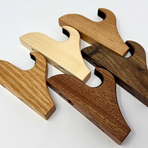 May include: Four wooden gun wall mounts in different wood types: maple, oak, walnut, and cherry. Each mount has a curved design and a black rubber insert for holding the gun.