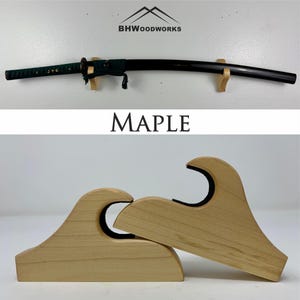 May include: A wooden wall mount for displaying a katana sword. The mount is made of maple wood and has a wave-like design. The text "MAPLE" is printed below the mount.