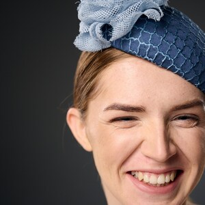 May include: A woman wearing a blue and light blue hat with a flower design. She is smiling and looking at the camera.