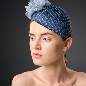 May include: A woman wearing a blue and light blue hat with a flower design. The hat is made of a textured fabric and has a rounded shape.