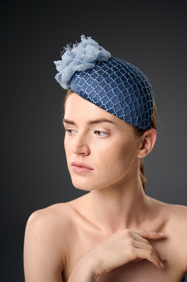 May include: A woman wearing a blue and light blue hat with a flower design. The hat is made of a textured fabric and has a rounded shape.